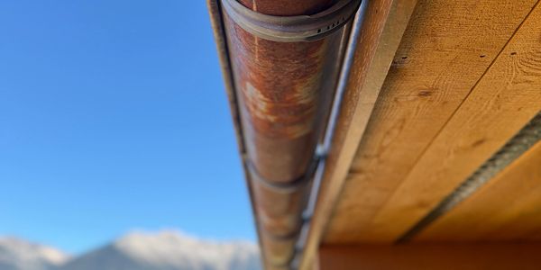 Rusty metal pipe attached to a wooden structure under a clear blue sky.