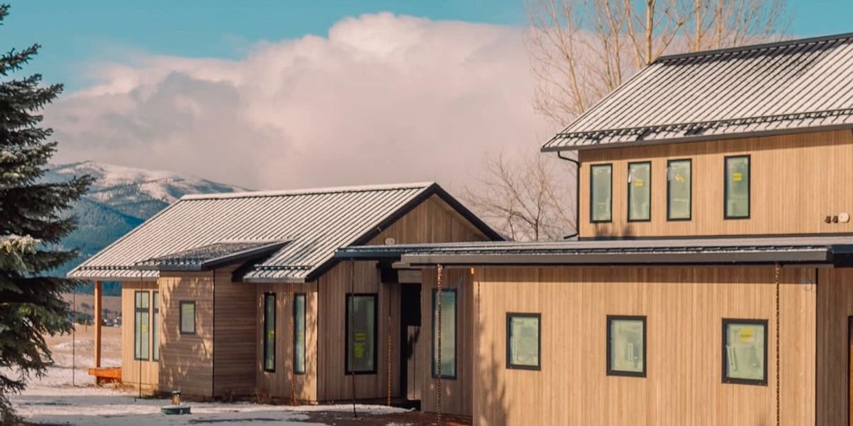 Modern wooden houses with snowy roofs under a clear sky.