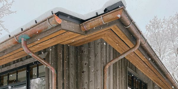 Snow falling on a wooden house corner with rusty gutters.