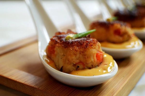 Crab cakes on spoons with sauce.