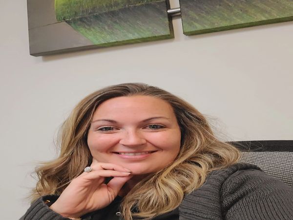 A smiling woman with wavy blonde hair sitting indoors.
