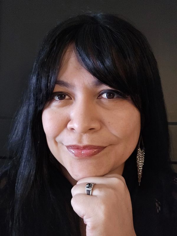 Woman with long dark hair resting her chin on her hand, wearing a ring and dangling earring.
