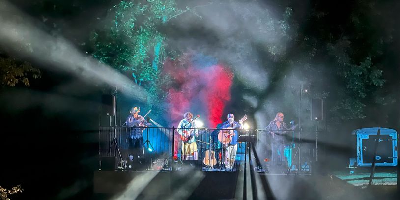 Band playing live outdoors with colorful lighting and fog effects.