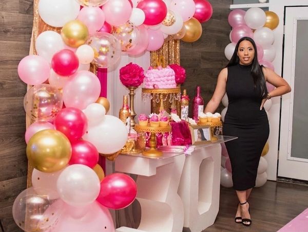 Woman in black dress posing by vibrant pink and gold birthday decorations.