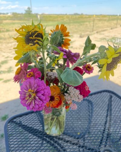 Bright bouquet of mixed flowers in a jar on an outdoor table.