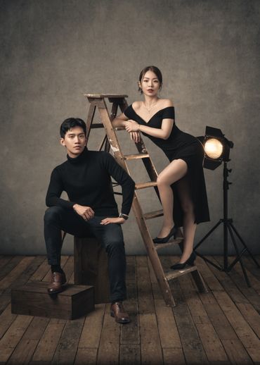 Stylish couple posing with a wooden ladder and vintage studio lighting.