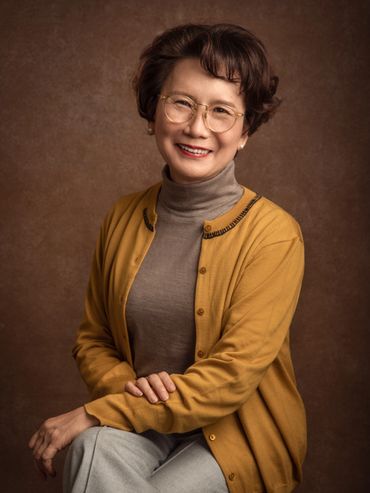 Smiling woman in glasses wearing a mustard cardigan and gray turtleneck.
