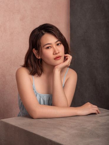 Young woman posing thoughtfully at a table with a two-tone backdrop.