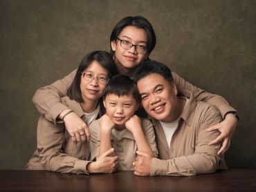 A happy family of four posing together in matching beige outfits.