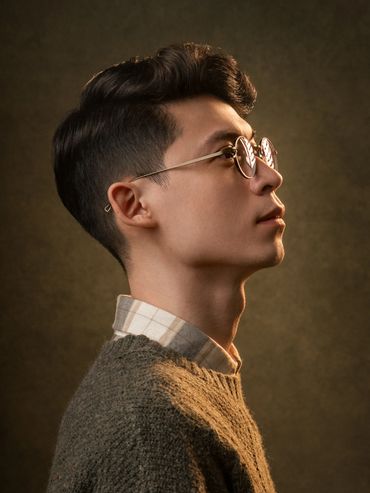 Profile portrait of a young man with glasses against a dark background.