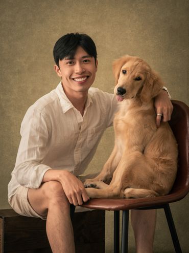 Young man smiling with his golden retriever sitting on a chair.