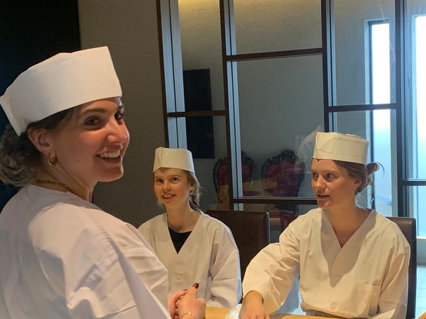 Three women in white chef uniforms and hats smiling indoors.