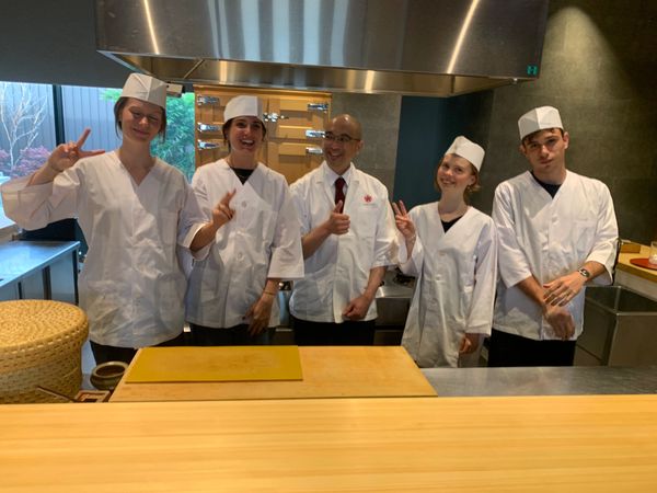 Five chefs in white uniforms posing happily in a kitchen.