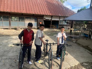 Three boys with bicycles outside a building.