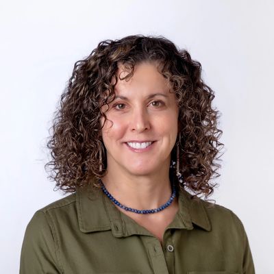 Smiling woman with curly hair wearing a green shirt and blue necklace.