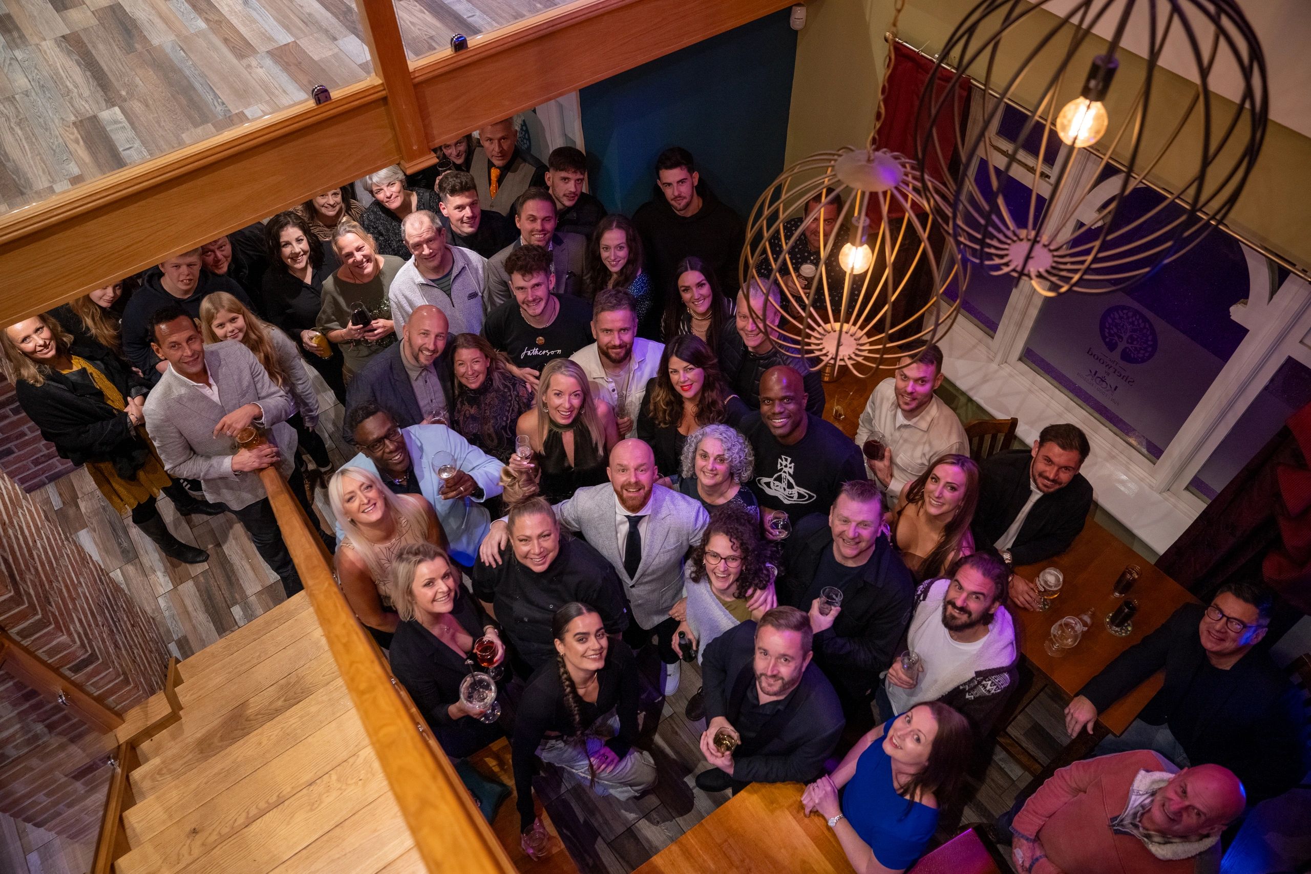 Large group of people smiling and holding drinks indoors.
