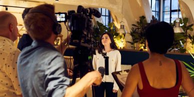 Woman being filmed by a camera crew indoors.