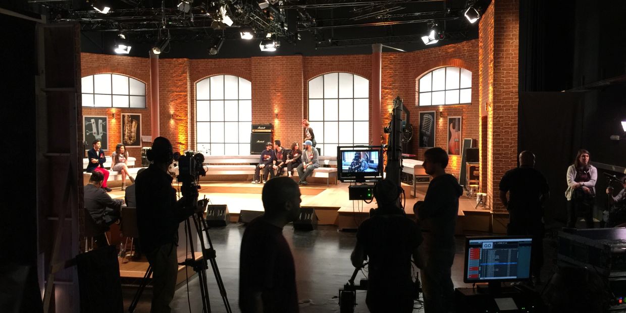 People filming a show on a lit stage inside a studio.