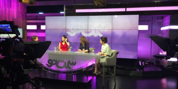 Women participating in a TV talk show on a purple-themed set.