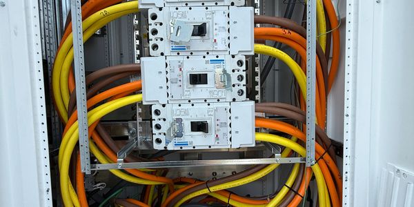 Electrical panel with multiple circuit breakers and colorful cables.
