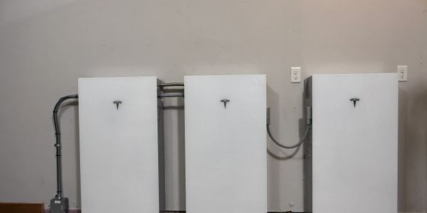 Three Tesla Powerwall units mounted on a wall with electrical wiring.