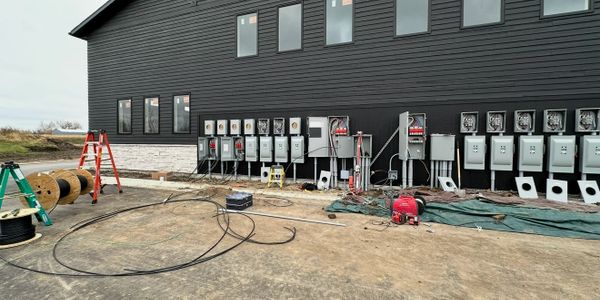 Electrical panels being installed on a black building exterior with cables and ladders around.