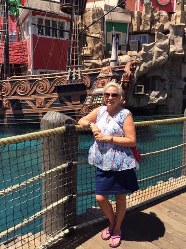 Woman posing by a wooden dock with a pirate ship in the background.
