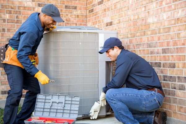 Two technicians appear to be working on an outdoor HVAC unit.