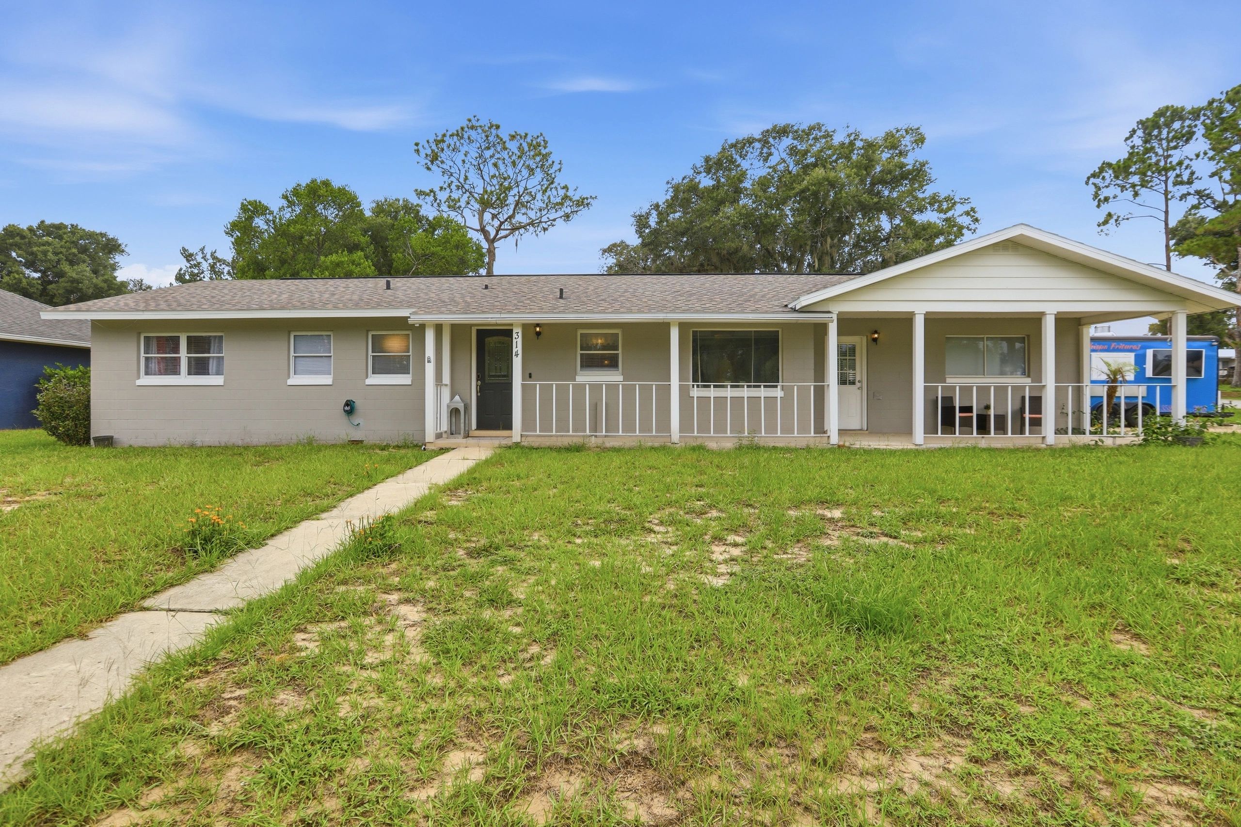 Single-story house with a large grassy front yard and blue sky.