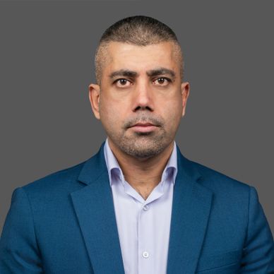 Serious man in a blue suit jacket and white shirt against a gray background.