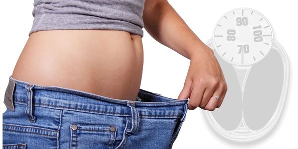 Person showing loose jeans indicating weight loss with a scale in the background.