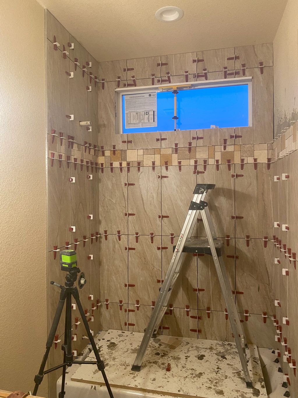Partially tiled bathroom shower area with tools and ladder.