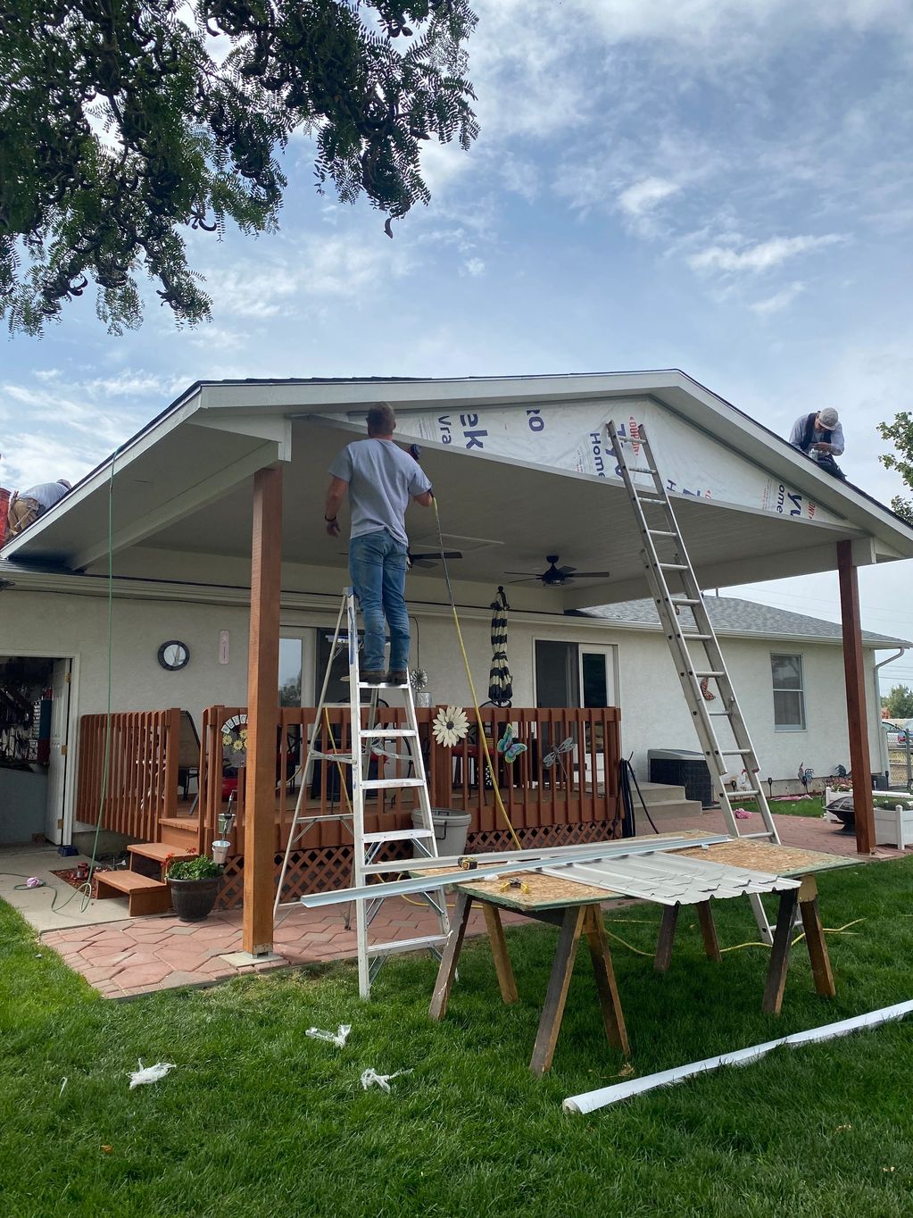 Workers renovating a porch roof with ladders and tools around.