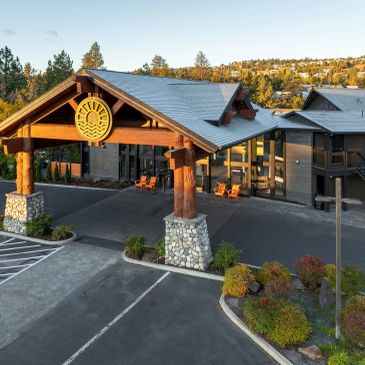 Wooden lodge entrance with stone pillars and parking area.