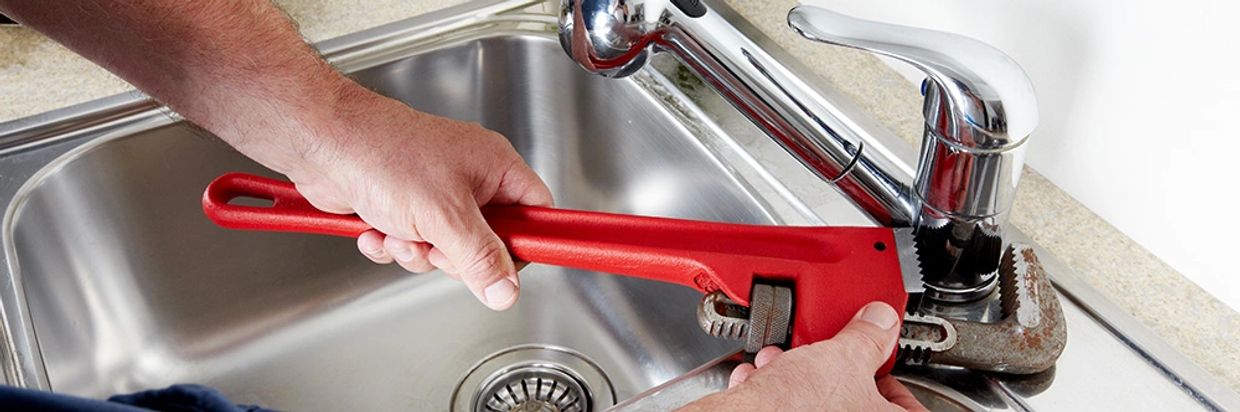 Plumber repairing old chrome kitchen faucet in airdrie home
