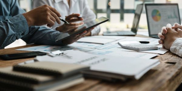 Two professionals discussing data on a tablet with charts and documents on the table.