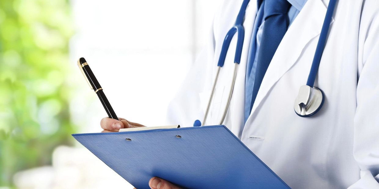 Doctor in white coat writing on a blue clipboard with a stethoscope.