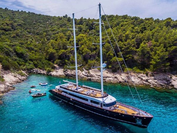 Luxury travel charter yacht. A large sailing yacht anchored near a lush, rocky shoreline while on luxury Croatia tours.