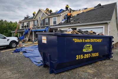 Workers repairing a roof with a dumpster in front.