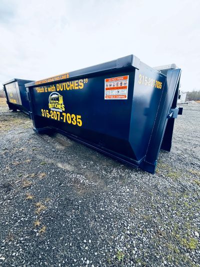 Large black dumpster with yellow text on gravel ground.