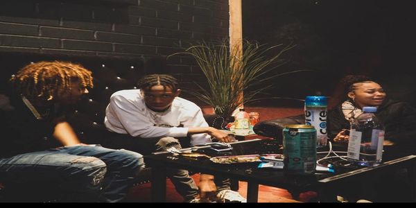 Three friends casually hanging out around a table with drinks and snacks.