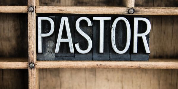 Letterpress blocks spelling "PASTOR" on wooden shelf.