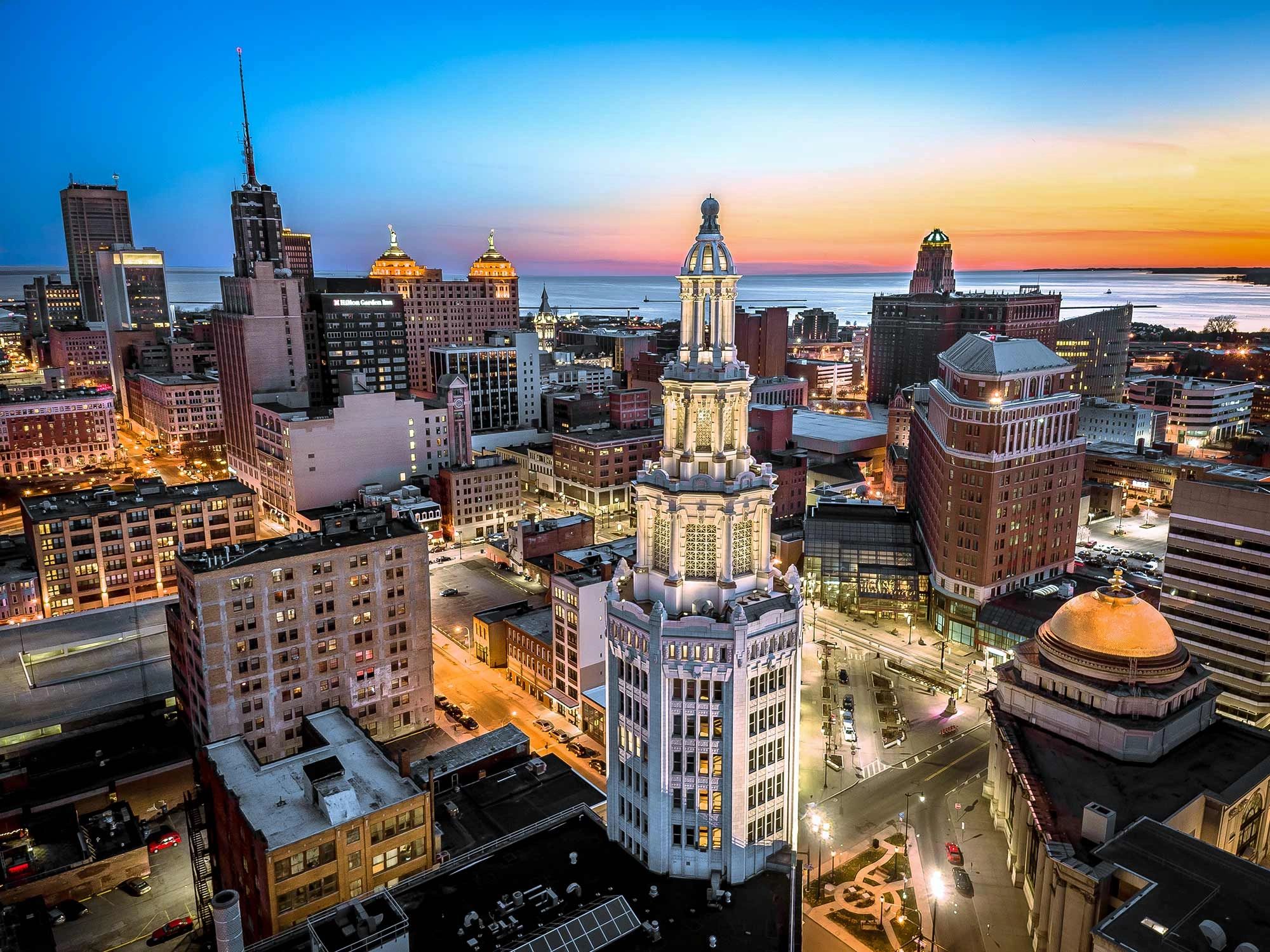Sunset view of a city skyline with illuminated buildings and waterfront.