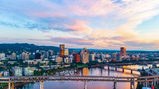 City skyline with bridges over a river during a colorful sunset.