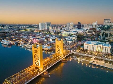 Golden hour view of a lit bridge over a river in a bustling city.