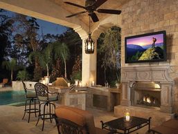 Cozy outdoor patio with fireplace and TV at dusk.
