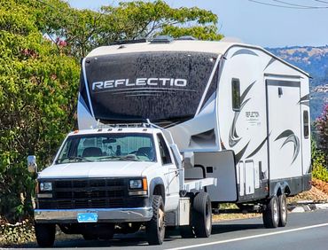 White pickup truck towing a Reflection RV camper on a sunny day.
