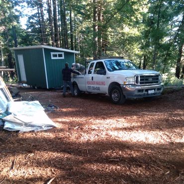 Truck and workers moving a small tiny home in a forest clearing.