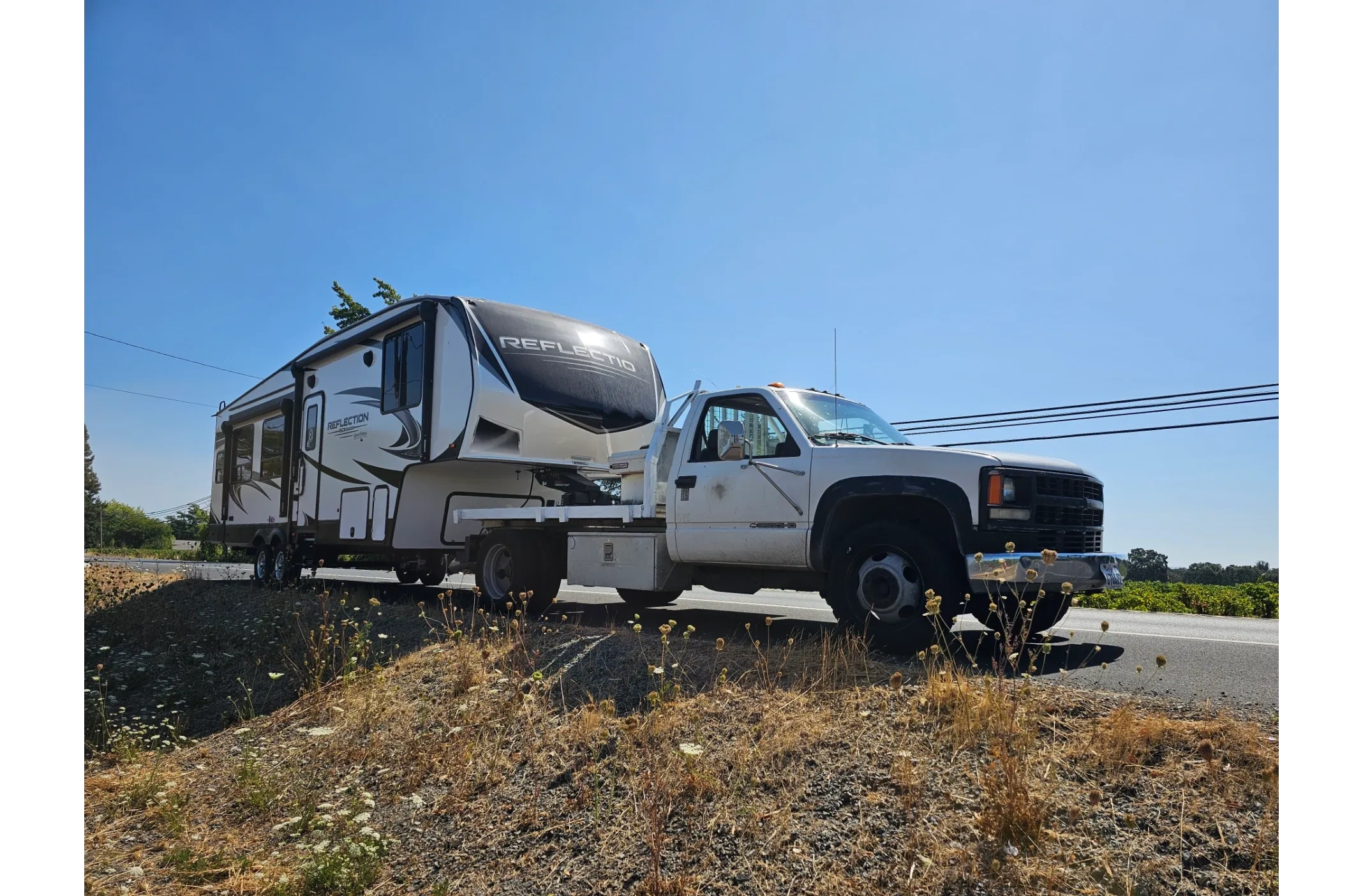 A white truck towing a large Reflection fifth-wheel trailer on a sunny day.