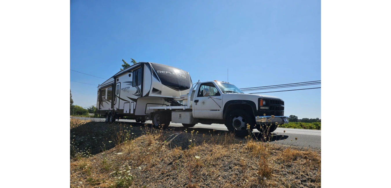 A white truck towing a large Reflection fifth-wheel trailer on a sunny day.